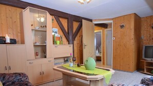 A cozy living room with wooden walls, a wooden table with a vase, a television, and a patterned sofa. - Gruppenausflug Nach Sebnitz (Sebnitz)
