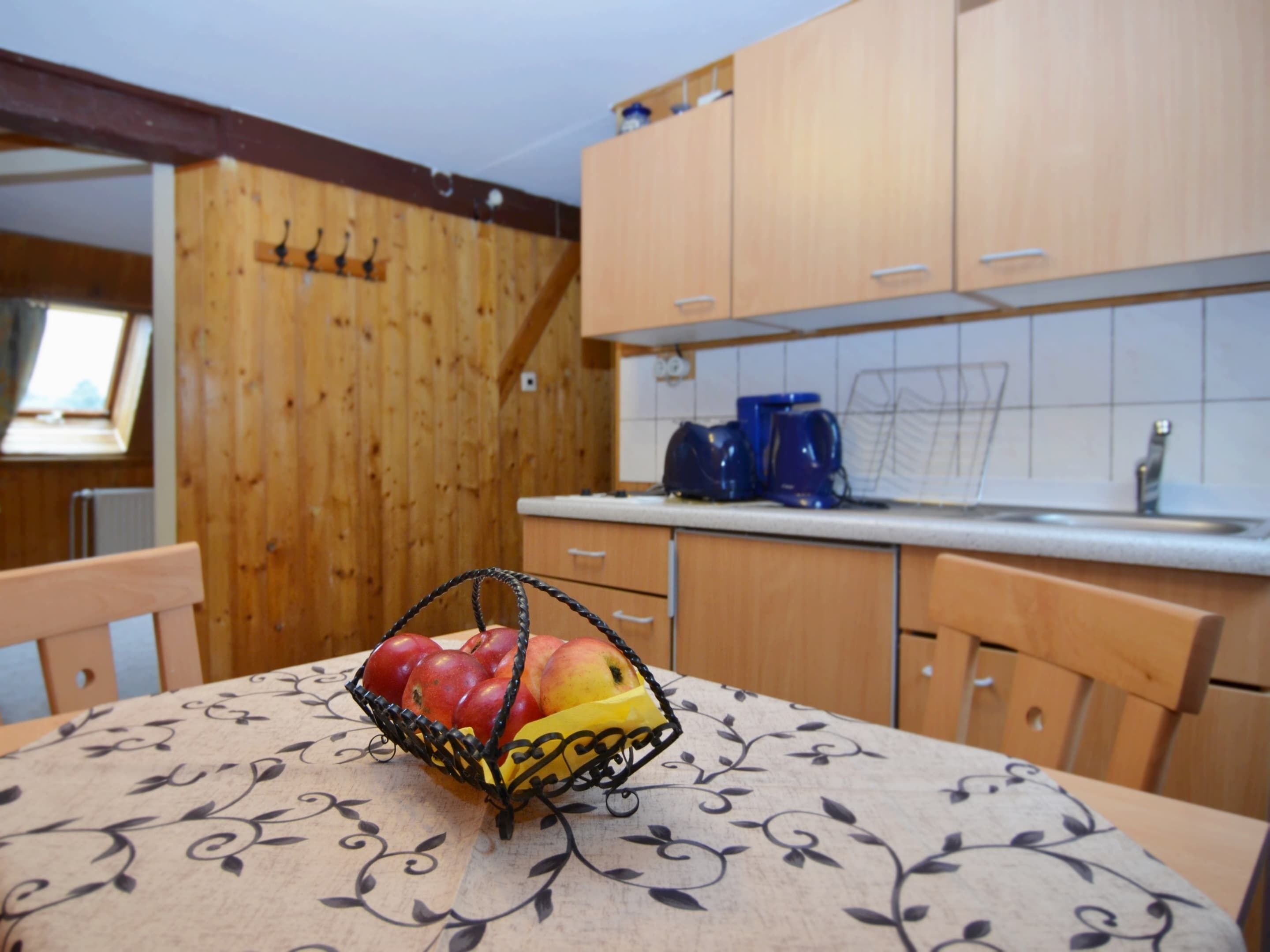 Une cuisine avec des meubles en bois, une machine à café et un panier de fruits sur la table.
