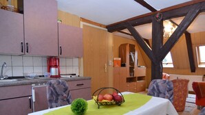 A dining area with a table set for two, a kitchen with pink cabinets, and a wooden ceiling structure. - Gruppenausflug Nach Sebnitz (Sebnitz)