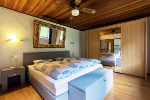 A bedroom with a large bed, a wooden ceiling, a ceiling fan, a nightstand, a bedside lamp, and a mirror.