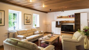 Un salon spacieux avec un plafond en bois, un ensemble de canapés, une table basse et un téléviseur.