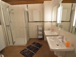 A bathroom with a glass-enclosed shower, two sinks, a mirror, and a towel rack.