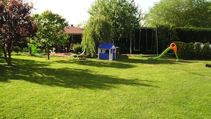 A grassy outdoor area with a small blue playhouse, a swing set, and a green slide. - Ferienwohnung mit Terrasse in Kropelin (Kroepelin)