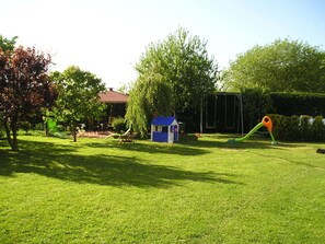 Enjoy a serene outdoor space with a lawn, playhouse, and swing set, surrounded by a tree and a hedge.