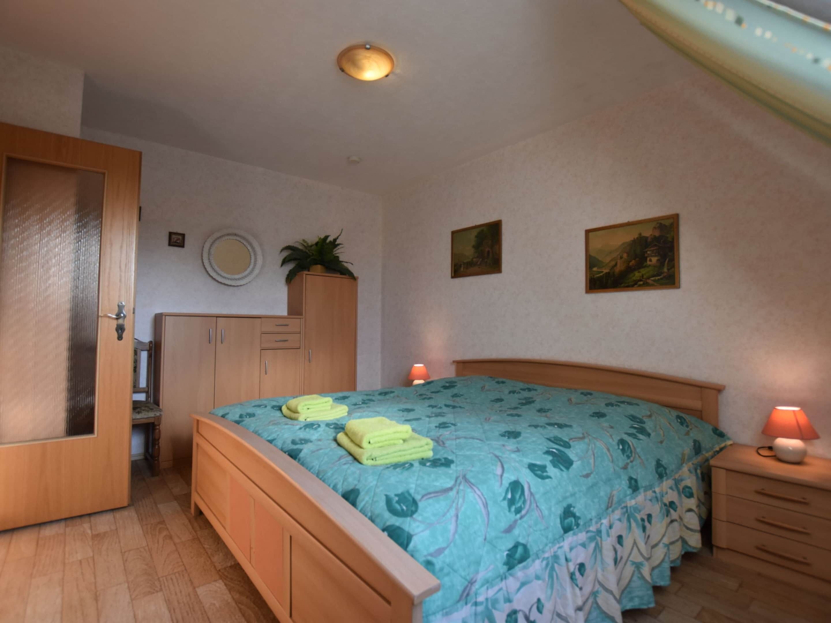 Une chambre à coucher avec un lit, une armoire en bois, des tables de chevet et un luminaire au plafond.