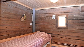 A small, wooden cabin room with a single bed, a window, and a wall-mounted light fixture.