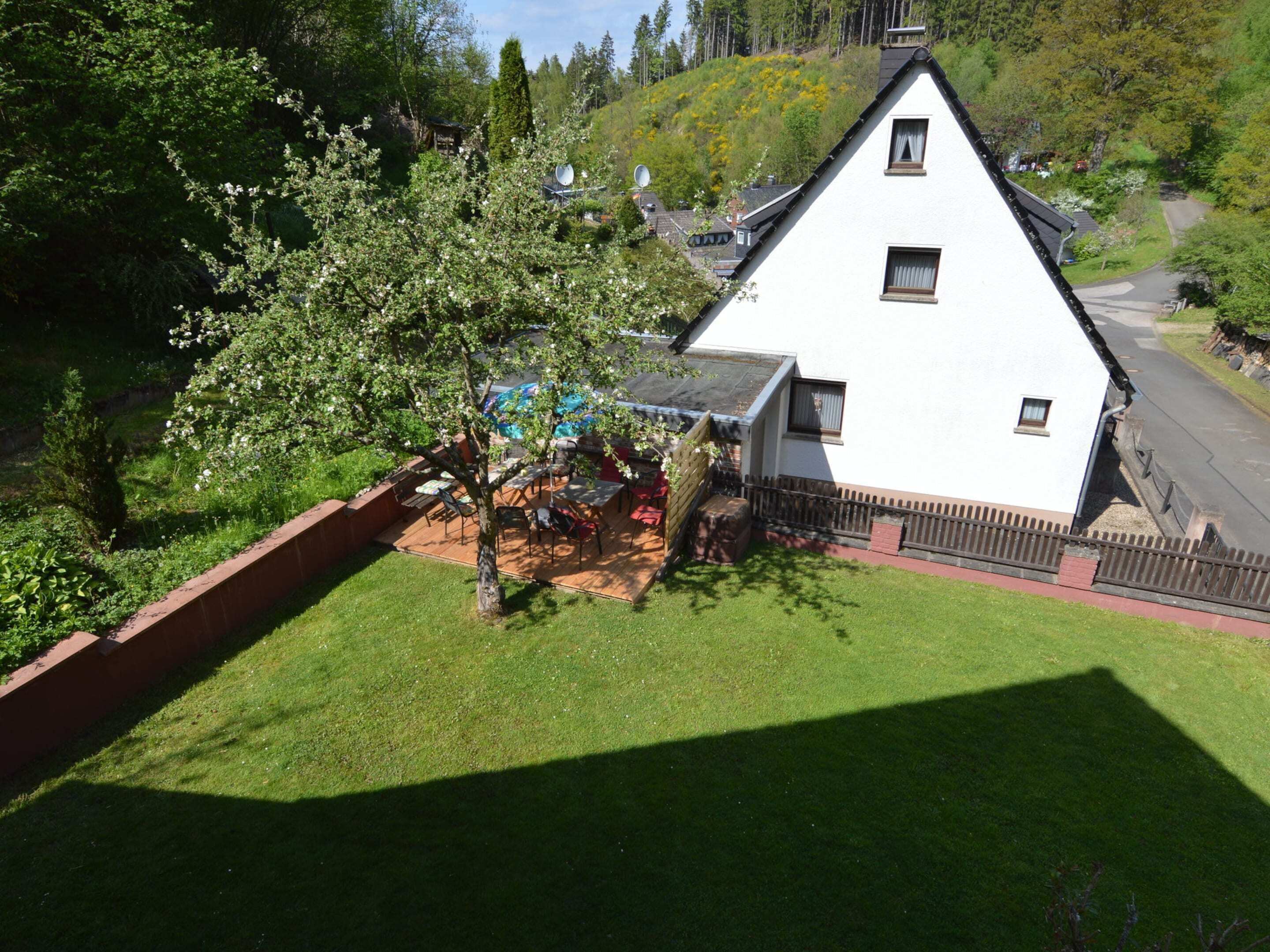 Ett vitt hus med ett sluttande tak, en inhägnad trädgård och ett träd framför.