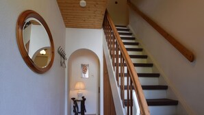 A staircase with wooden handrails and a white wall with a round mirror and a small table with a lamp. - Hellenthal Family Retreat (Hellenthal)