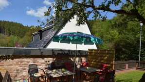 A patio with a brick wall, a table, chairs, and a green umbrella. - Hellenthal Family Retreat (Hellenthal)