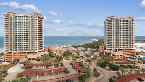 Un hotel de gran altura con varios balcones, un área de estacionamiento y vista a la playa y al océano.