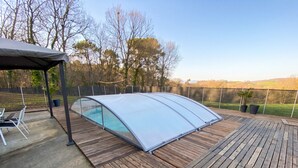 Un espace extérieur abrité comprenant une piscine, une terrasse en bois et une pergola.