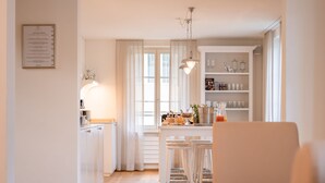Une cuisine moderne avec des meubles blancs, un coin repas doté de tabourets de bar et une bibliothèque intégrée agrémentée d’objets décoratifs.