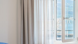 Une chambre à coucher avec un lit, une fenêtre donnant sur un plan d’eau et des montagnes, et un rideau.