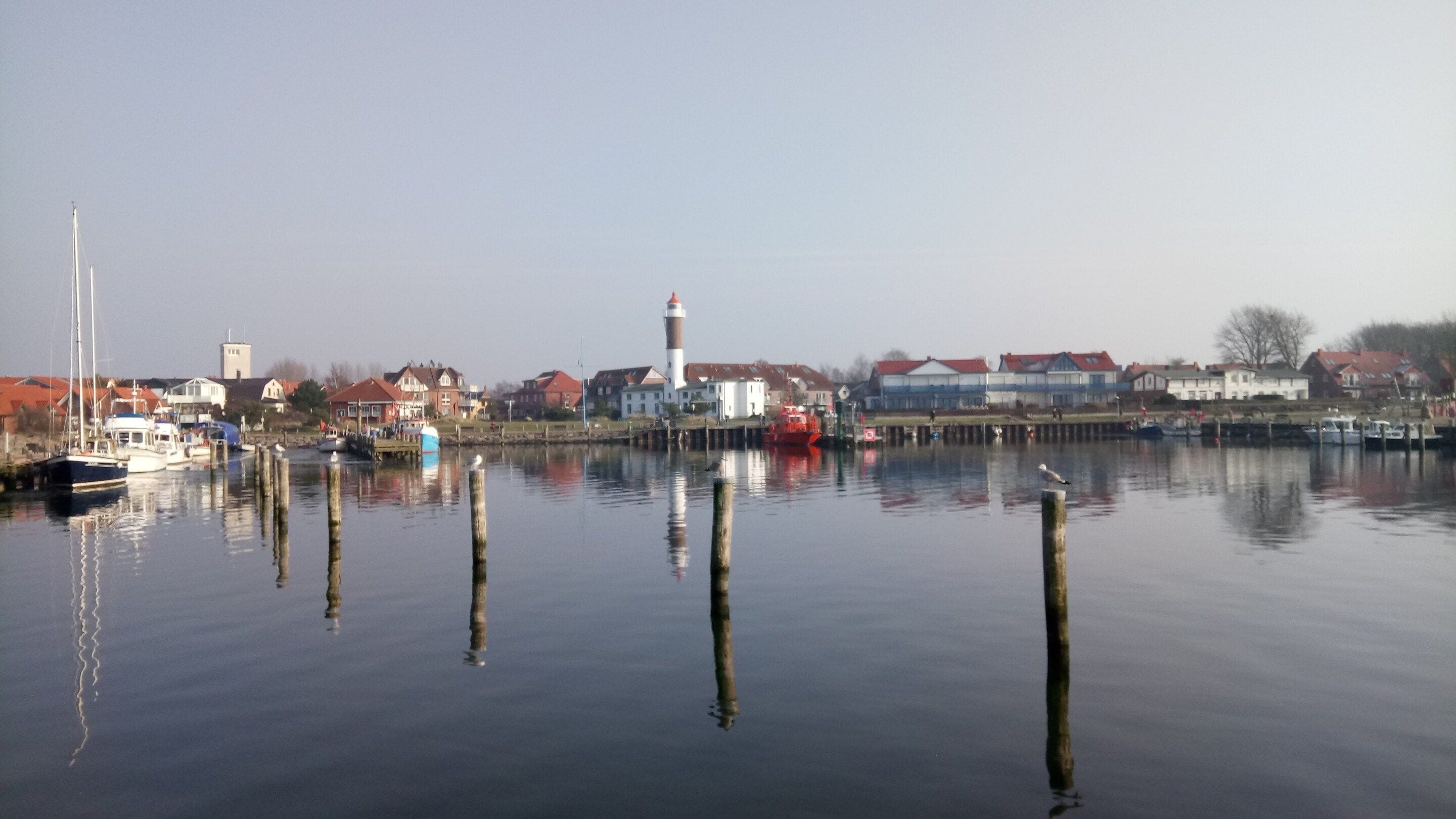 A calm harbor with boats, a lighthouse, and buildings along the shore.