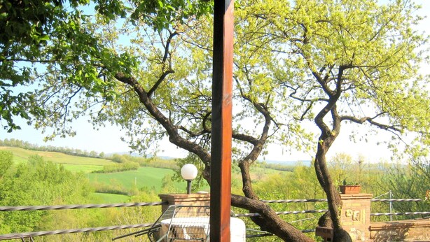A patio with a metal chair and a table, overlooking a green landscape with trees and a hill. - Tuscan Charm: Frassini Cottage (Chiusdino)
