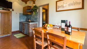 A wooden dining table with chairs, a kitchen area with a brick stove, and a framed cityscape artwork on the wall. - Tuscan Mansion Getaway (Castelfranco Piandisco)