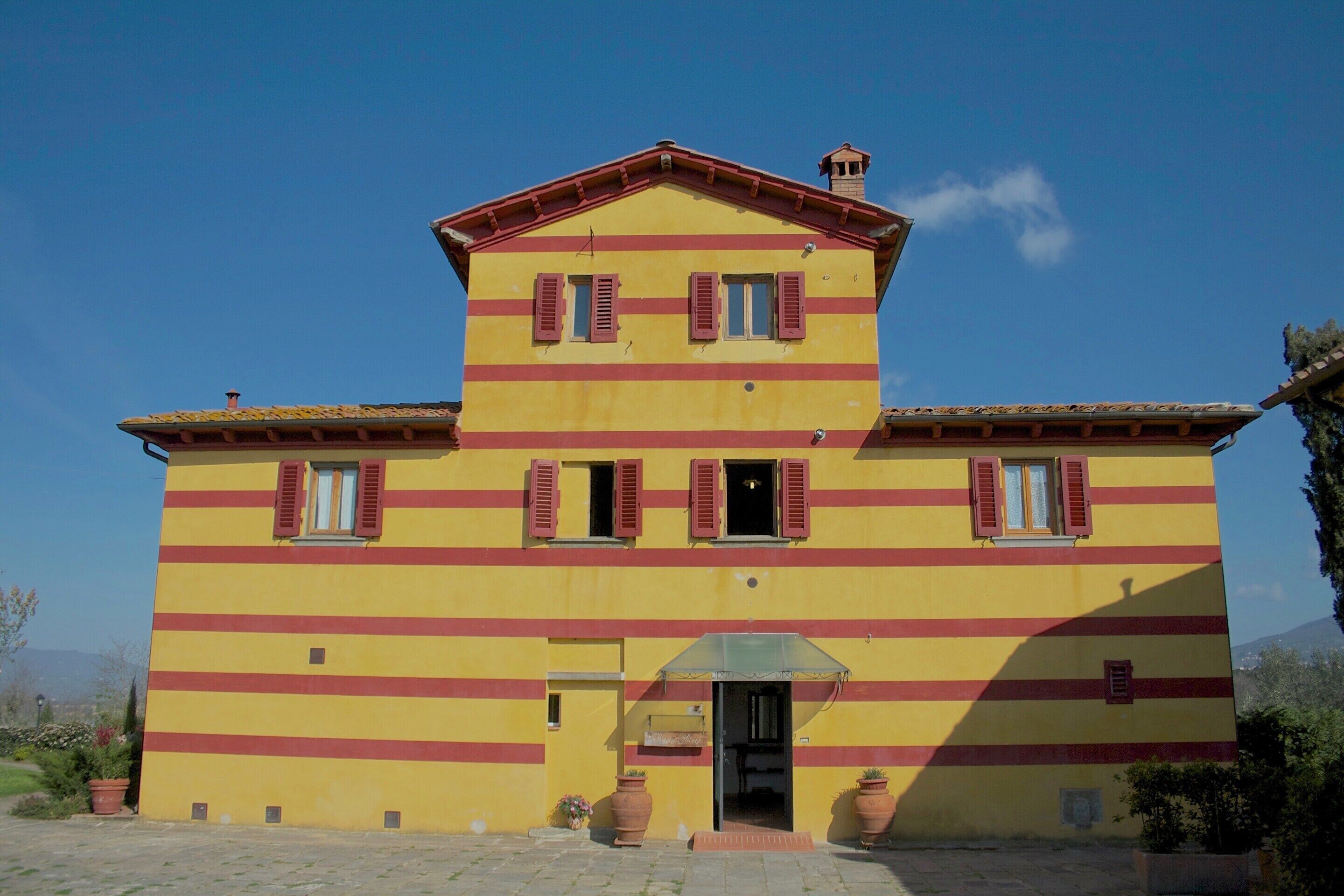 A two-story building with a yellow facade and red window shutters.