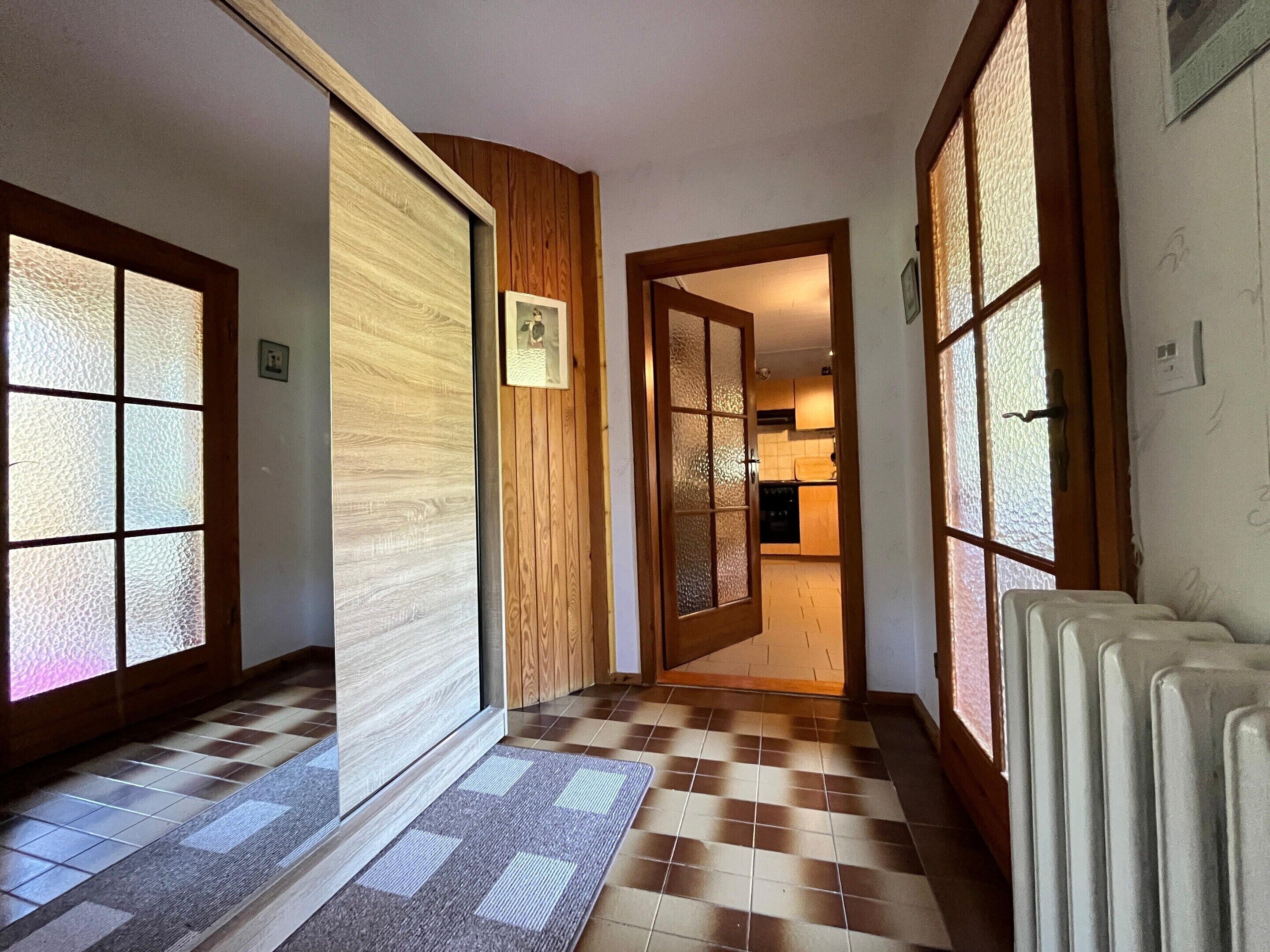 A hallway with a checkered floor, wooden paneling, and frosted glass doors leading to a kitchen area.