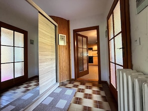 A hallway with a checkered floor, wooden paneling, and frosted glass doors leading to a kitchen area. - Cozy Apartment near Sea in Warin (Warin)