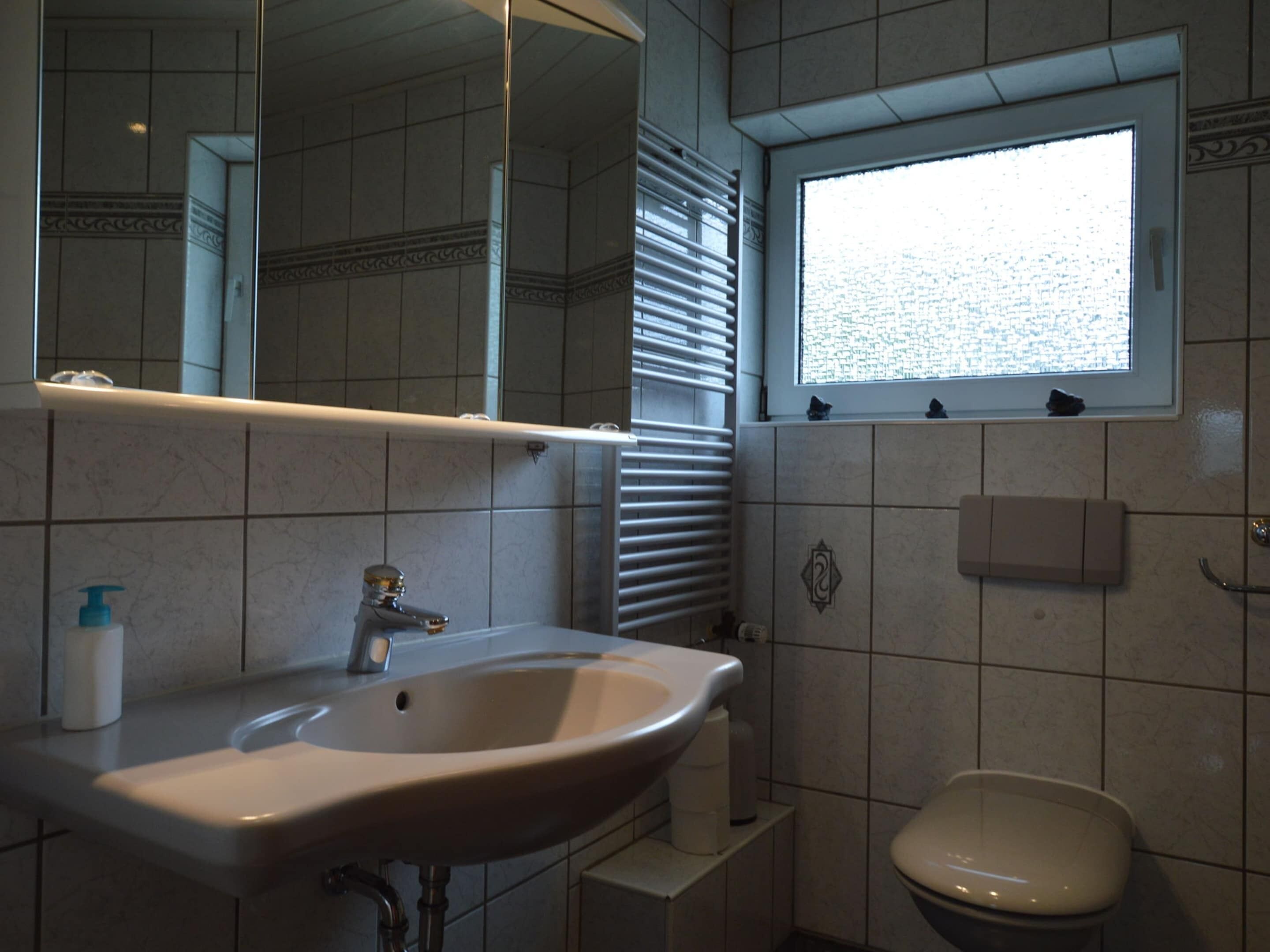 Ein Badezimmer mit Waschbecken, Spiegel, Fenster und Toilette.