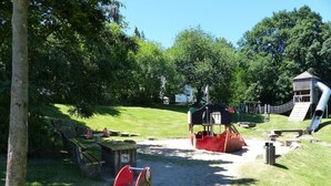 Un parque infantil con una estructura de juegos con temática de barco, un tobogán y columpios.