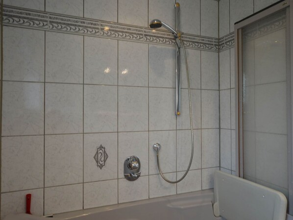 A bathroom with a bathtub, a shower with a handheld showerhead, and a wall-mounted faucet.