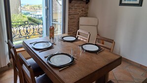 Mesa de jantar posta com pratos, talheres e copos, com vista para o mar através de uma janela.