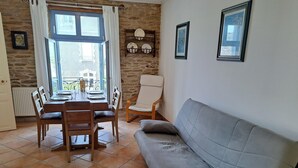 Uma área de refeições com mesa e cadeiras, um sofá cinza e uma parede de pedra com quadros emoldurados.