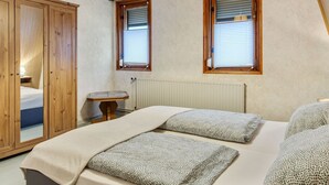 A bedroom with a bed, two windows with blinds, a wooden wardrobe, a bedside table, and a hanging light fixture. - Holiday Home in Thuringia With Private Terrace, use of a Garden and Pool (Roemhild)