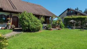 A residential property with a well-maintained lawn, a wooden porch, and a small garden area. - Ferienwohnung in Gutenbach (Guetenbach)