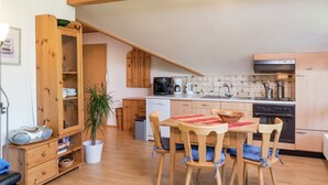A compact kitchen with wooden cabinets, a dining table with chairs, a coffee maker, and a dishwasher. - Ferienwohnung in Gutenbach (Guetenbach)