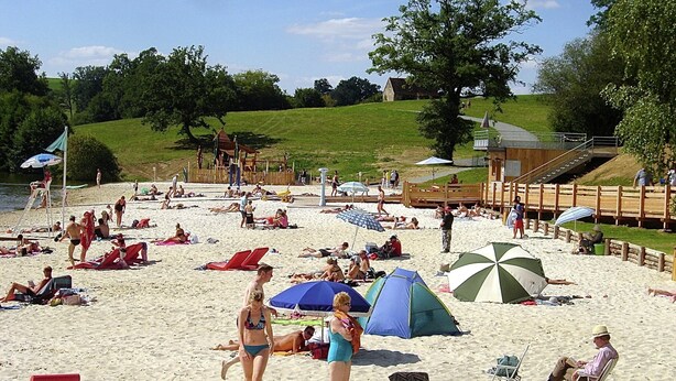 A beach with people sunbathing, umbrellas, and a tent. - Peaceful Cottage in Savignac for 2 (Savignac-Ledrier)