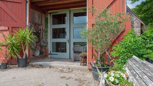 A red building with a wooden bench and potted plants. - Farmhouse by Lauwers River With Rowing Boat (Burum)