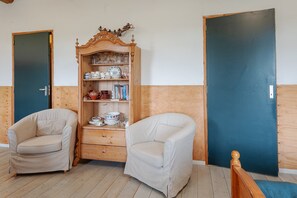 Une pièce avec deux fauteuils beiges, un buffet en bois contenant de la vaisselle et deux portes.