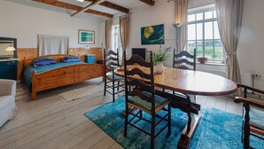 A room with a wooden bed, a dining table with chairs, a window with curtains, and a painting on the wall. - Farmhouse by Lauwers River With Rowing Boat (Burum)