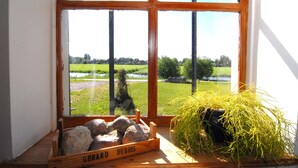 A window with a view of a grassy field and a river. - Farmhouse by Lauwers River With Rowing Boat (Burum)