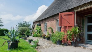 A brick building with a red door, a cobblestone pathway, and potted plants. - Farmhouse by Lauwers River With Rowing Boat (Burum)