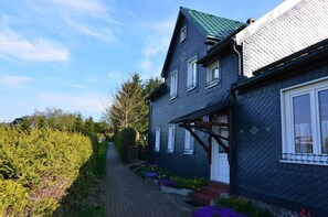 Une maison à deux étages, avec un toit sombre et des encadrements de fenêtres blancs, un chemin pavé et un jardin fleuri.
