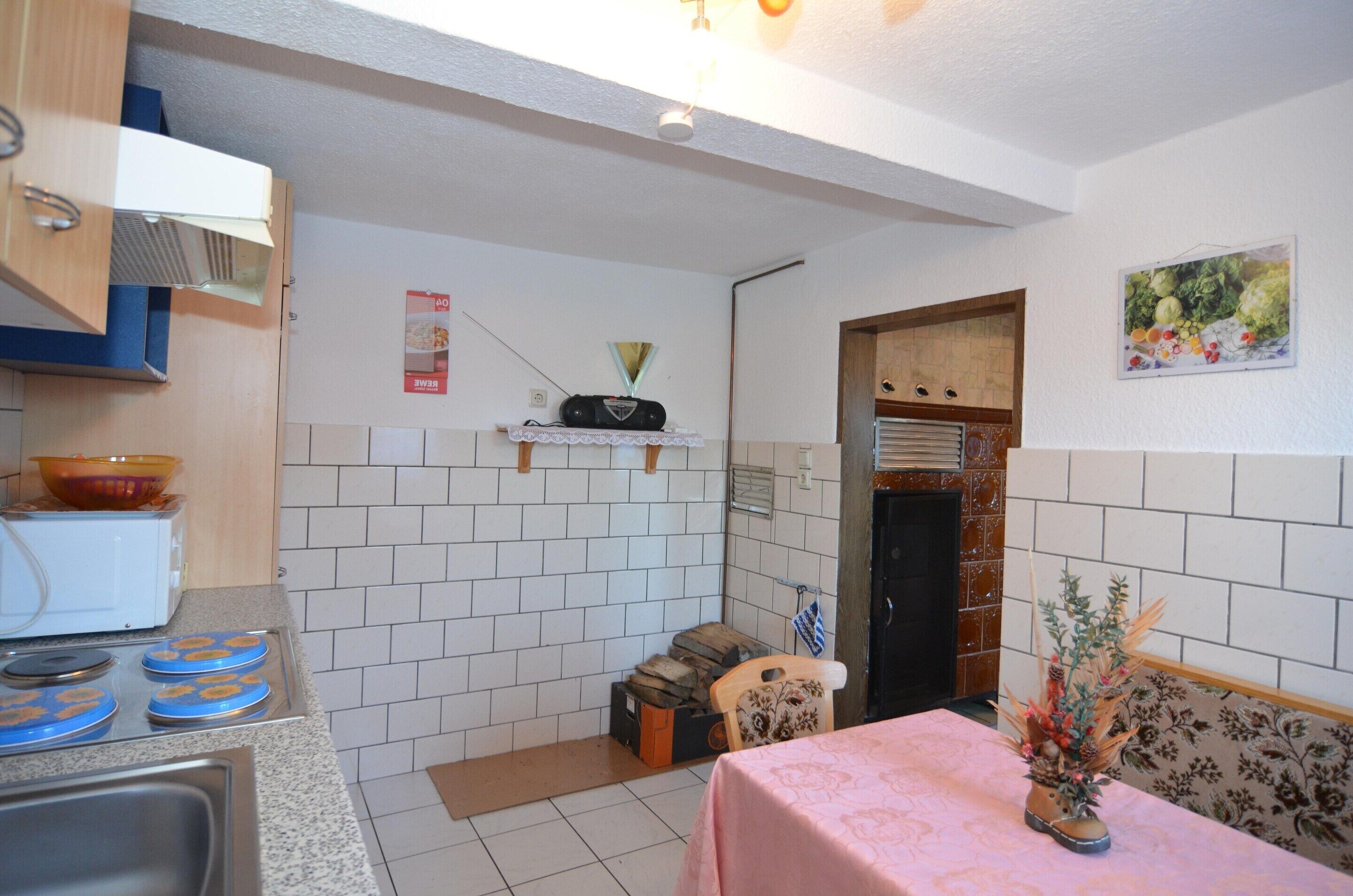 Una cocina con paredes de azulejos blancos, una estufa, un microondas y una mesa con mantel rosa.