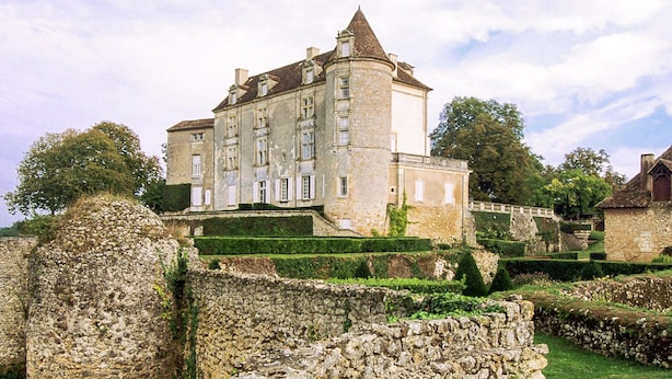 A historic stone building with a central tower, surrounded by well-maintained gardens and a stone wall.