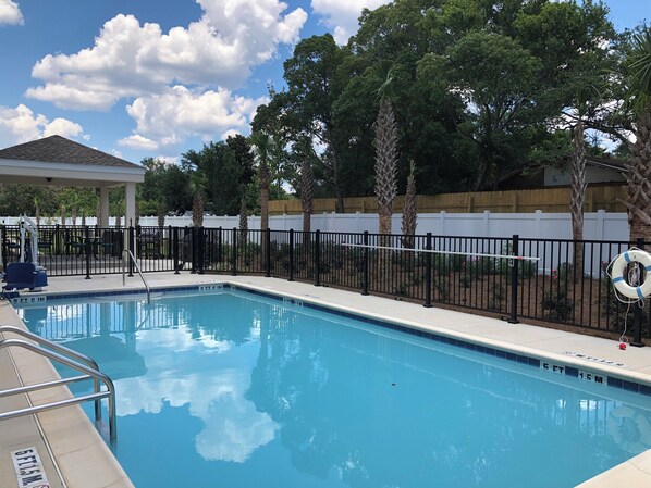 A swimming pool with a fenced deck area, surrounded by trees and a wooden fence.