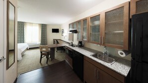 A compact hotel room with a kitchenette, a bed, a chair, and a desk. - Candlewood Suites Panama City Beach Pier by IHG (Panama City Beach)