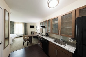 A compact hotel room with a kitchenette, a bed, a chair, and a desk.
