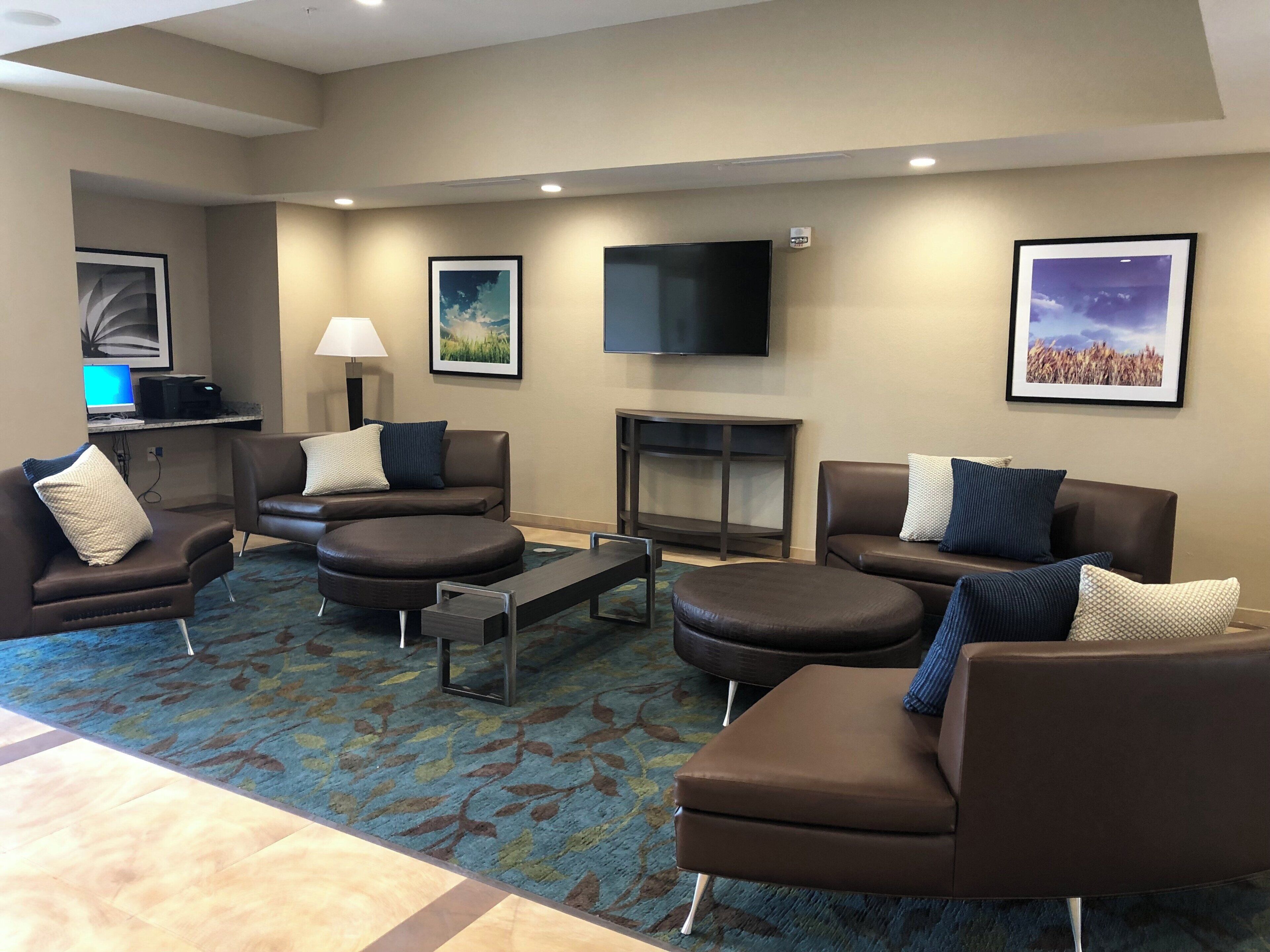 A hotel lobby with leather sofas, a flat-screen TV, framed artwork, and a desk with a computer.