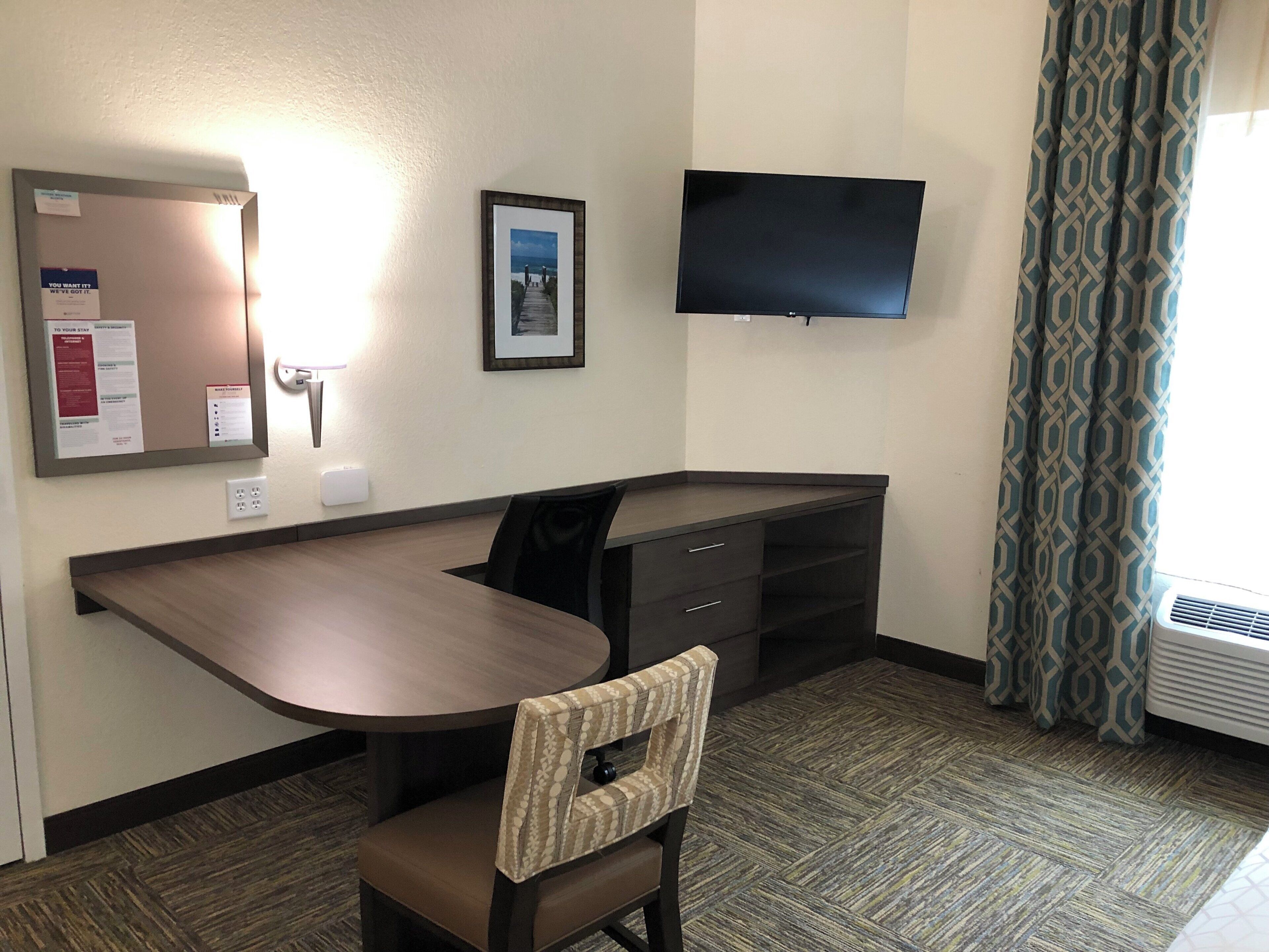 A hotel room with a desk, chair, TV, and a window with curtains.
