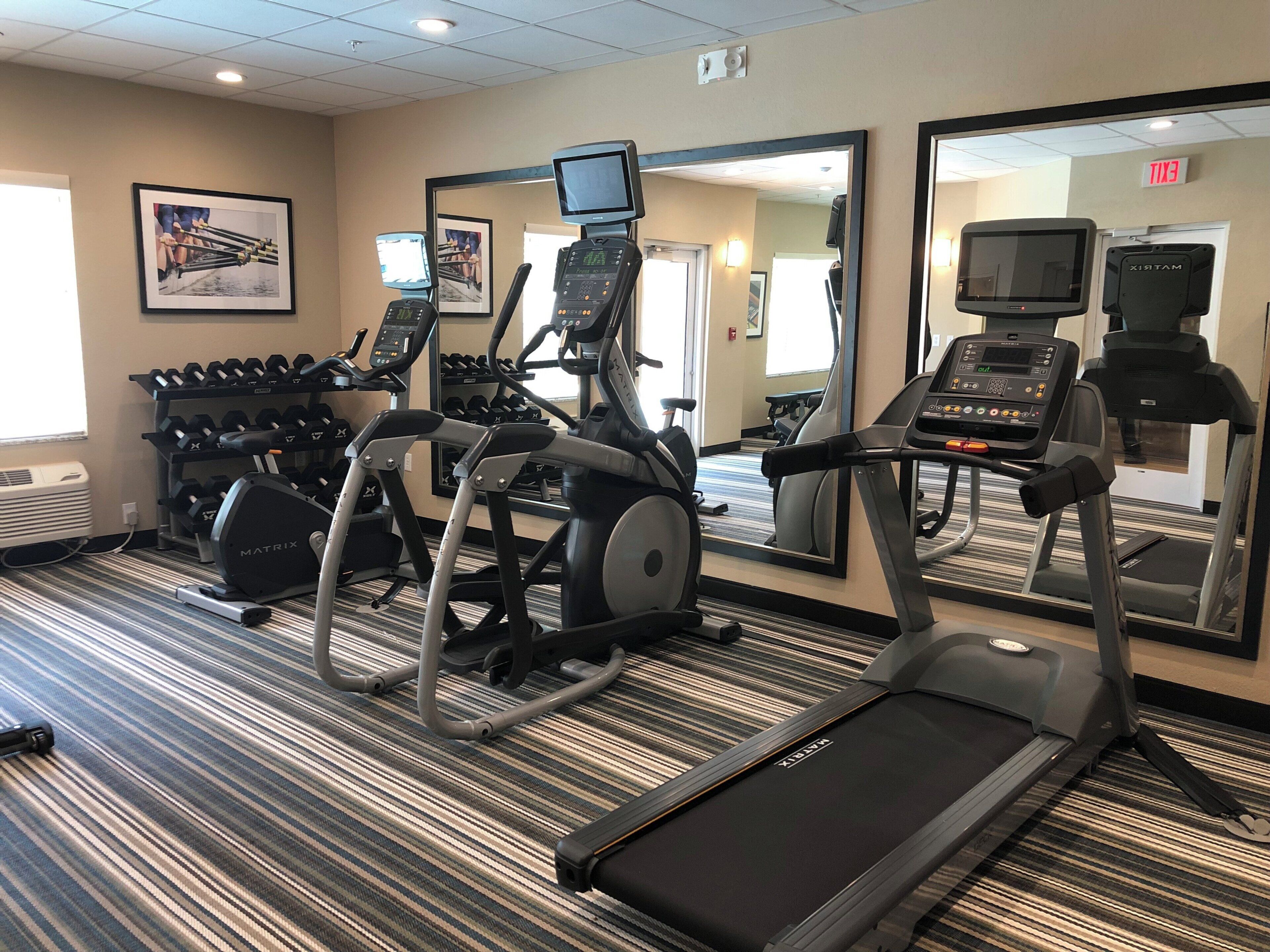 A hotel gym with treadmills, elliptical machines, and a mirror wall.