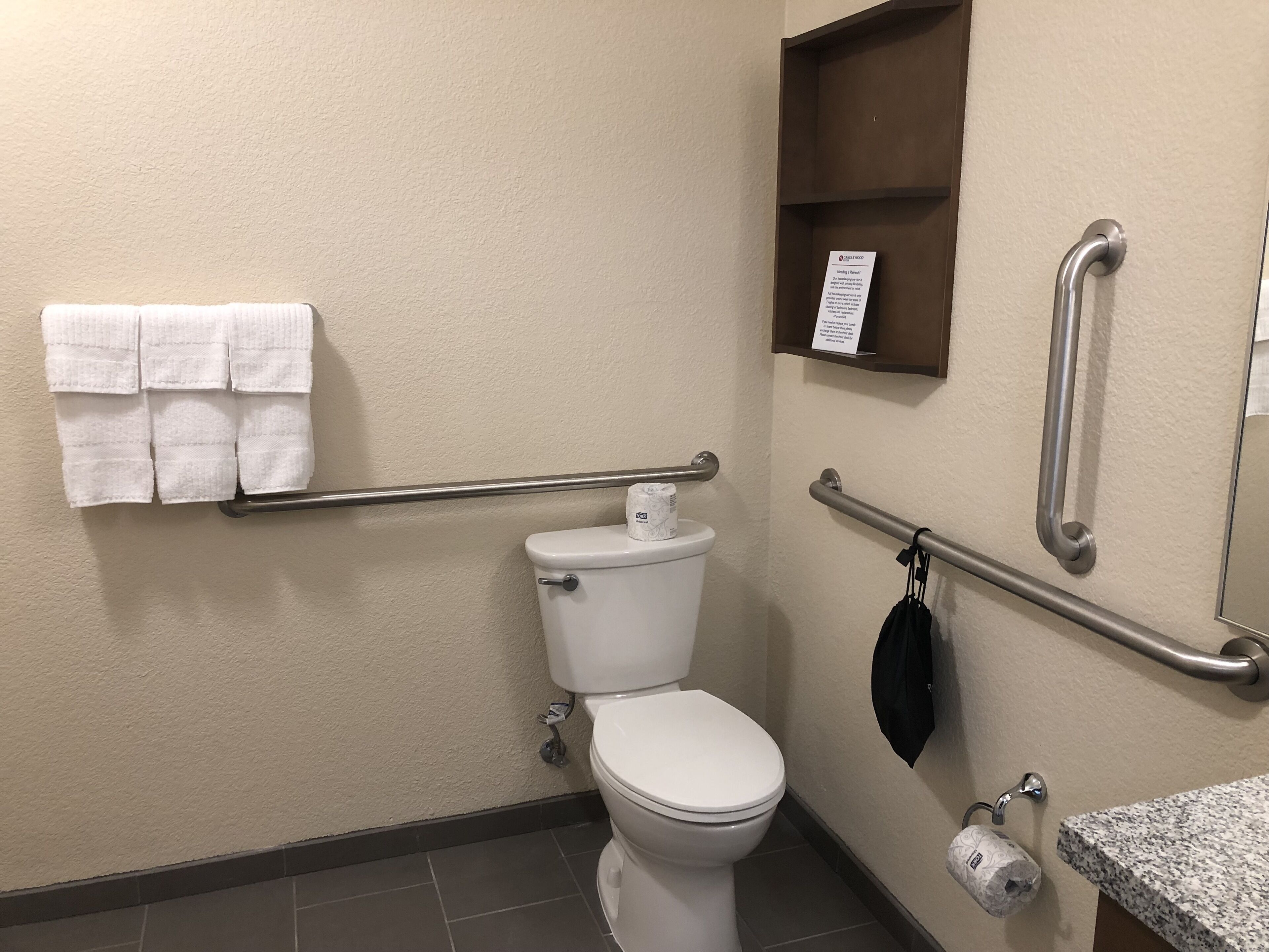 Une salle de bain équipée de toilettes, de barres d’appui, d’un porte-serviettes et d’un distributeur de serviettes en papier.