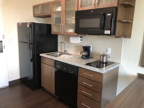 Cozinha compacta equipada com geladeira, micro-ondas, cafeteira, pia e lava-louças.