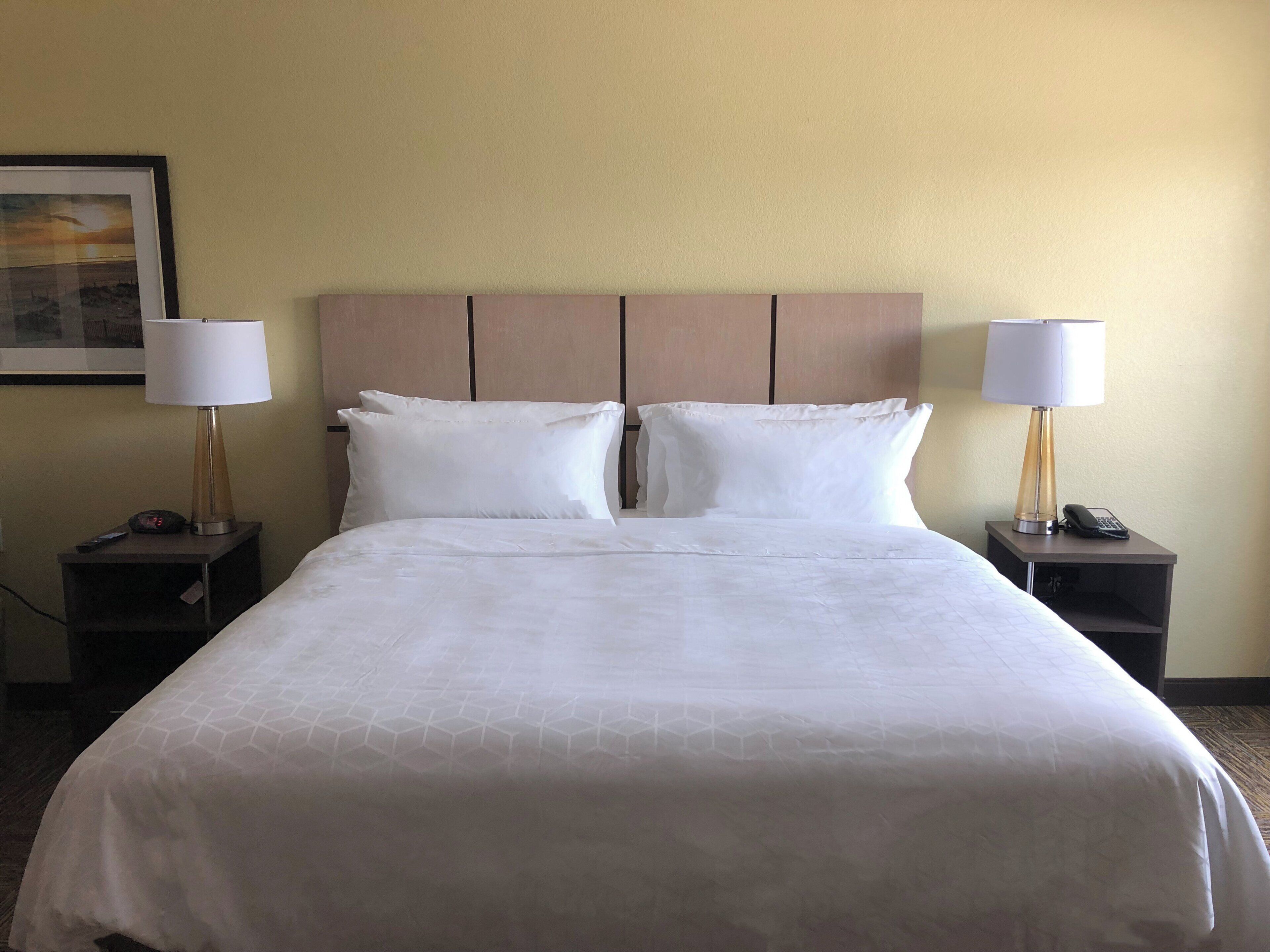 A hotel room with a large bed, two bedside tables with lamps, a clock, and a painting on the wall.
