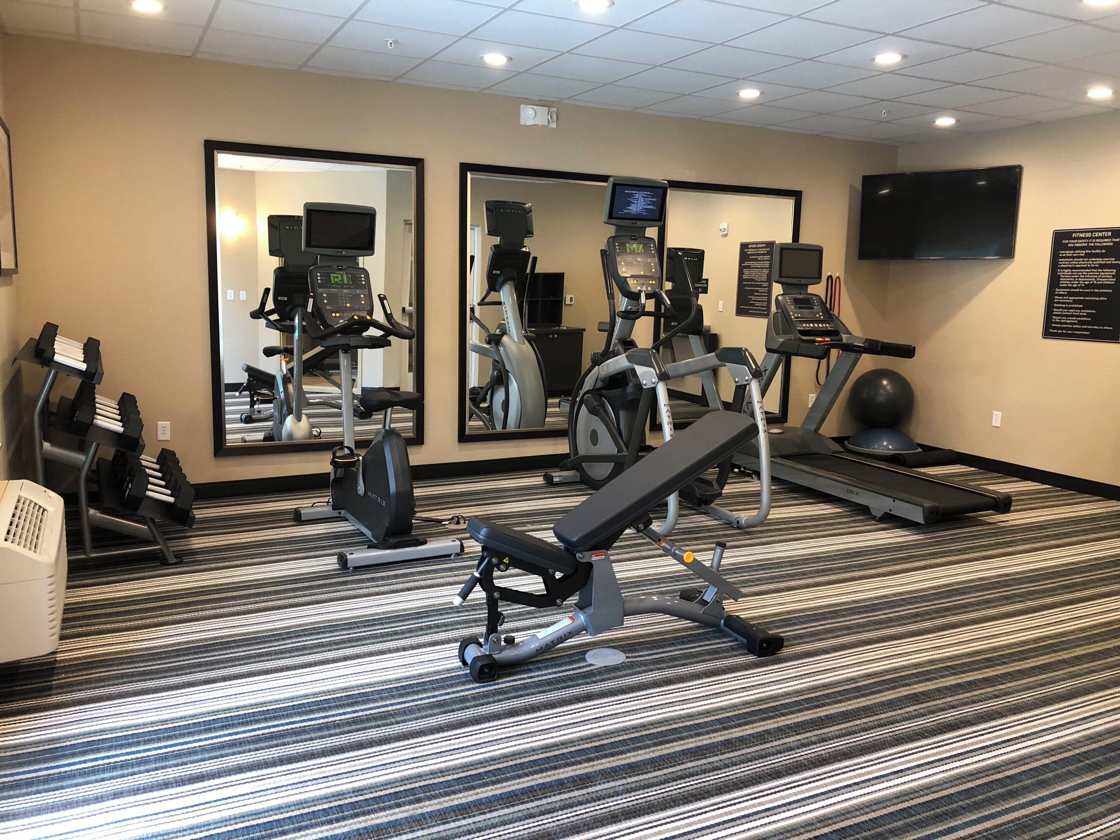 A fitness center with treadmills, an elliptical, a bench press, and a mirrored wall.
